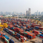 Cargo containers at a major shipping port handling trade logistics crucial for national car production exports.