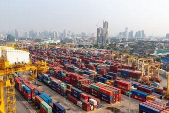 Cargo containers at a major shipping port handling trade logistics crucial for national car production exports.